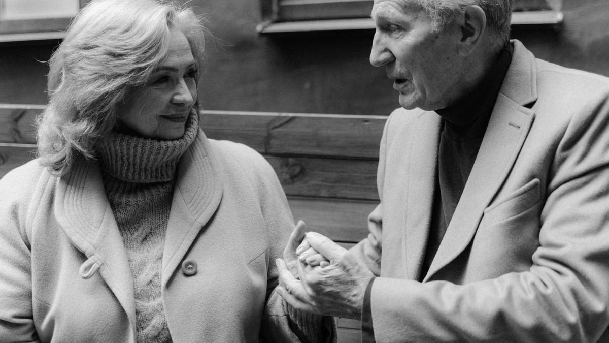 Black and white photo of an elderly couple sharing a moment, holding hands and connecting.